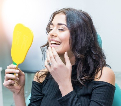 woman checking smile in mirror after cosmetic dentistry