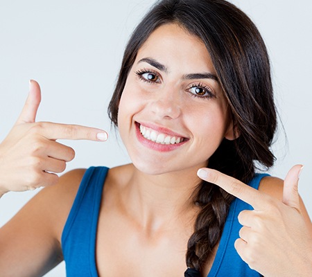 young woman smiling and pointing to her teeth 