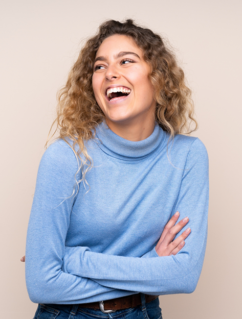 Young woman in a blue sweater smiling with dental crowns in Bowie