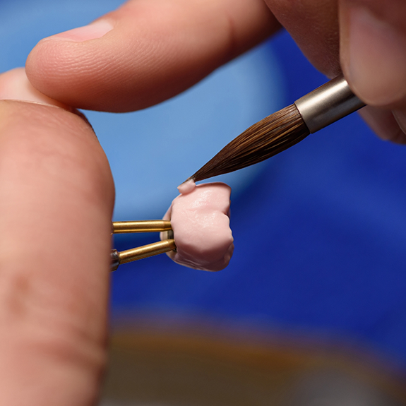 Close up of a person painting a dental crown with a tiny brush