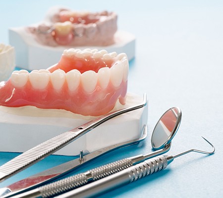 dentures sitting on a mold of a mouth next to dental instruments