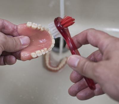 a person cleaning their dentures with a denture brush
