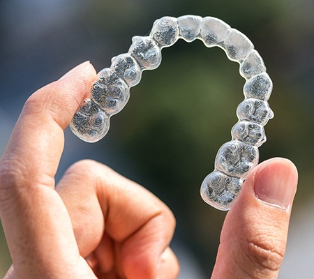 Hand holding up Invisalign in Bowie aligner 