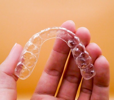 An individual holding a clear aligner designed to straighten teeth