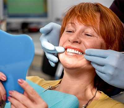 woman checking smile in blue mirror during dental checkup