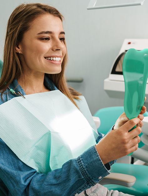 Woman looking at her smile in a mirror after restorative dentistry in Bowie