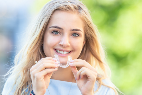 blonde woman smiling holding invisalign tray
