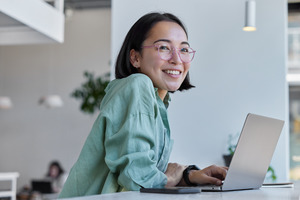 Woman with glasses smiling while typing on laptop